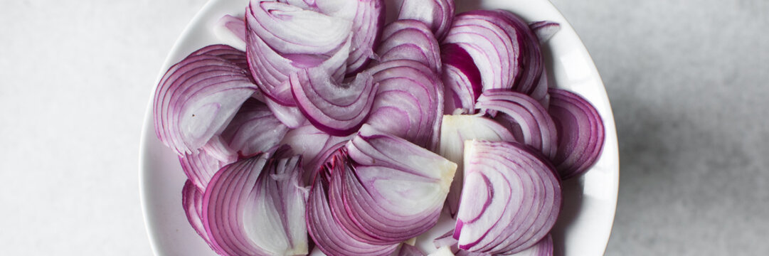 Thinly Sliced purple onions on a white plate, red onions sliced for cooking