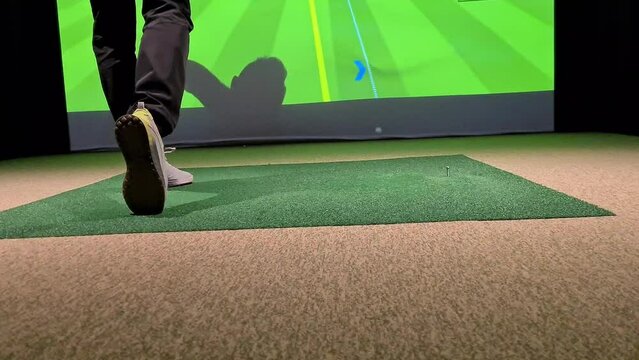 Professional male golfer playing golf indoors in golf simulator closeup. training field with screen