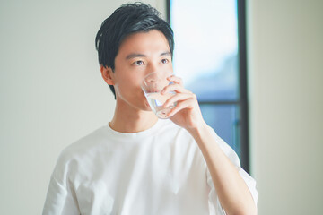 コップに入った水を飲んで水分補給をする若い男性