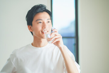 コップに入った水を飲んで水分補給をする若い男性