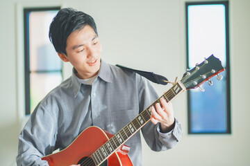 自宅でアコースティックギターを弾く若い男性