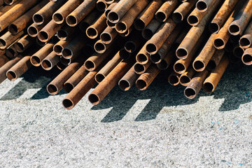 Iron pipes for gasification or water supply lie in pile on concrete outside on street on summer day. Background..