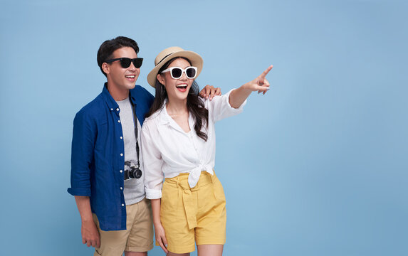 Happy Asian couple tourist hand pointing to copy space with going to travel on holidays isolated on blue background.