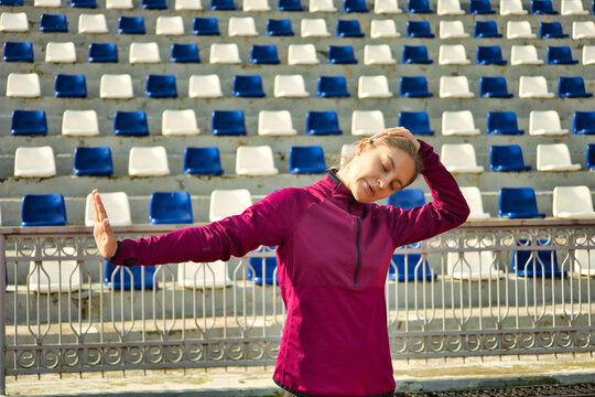 Sports runner girl at the stadium. Photo of a young girl in fashionable sportswear. Dynamic movement with exercises. Sport, motivation and healthy lifestyle