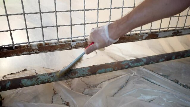 Process of removing rust from metal surface with steel brush, worker grinding eroded steel frame before restoration process, old rusty metal gate on construction site, rubbing corroded layer of steel