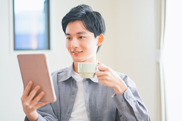 ソファでコーヒーを飲みながらタブレットを見る若い男性