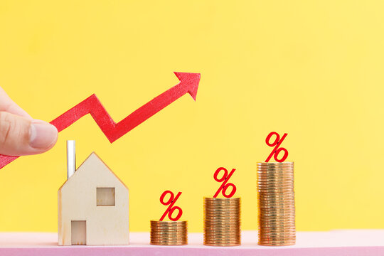 Woman hand hold a red arrow graph and home and percent put on the stack gold coin on bright yellow color background, Saving money for buy house and loan to business investment for real estate concept.