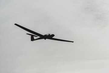 The silhouette of a two-man glider flying overhead against the sky.
