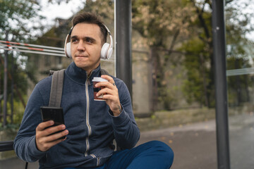 One man young adult male sit at public transport bus station waiting