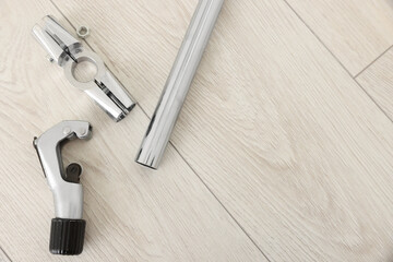 Modern metal wrench and pipe on wooden floor, top view. Space for text