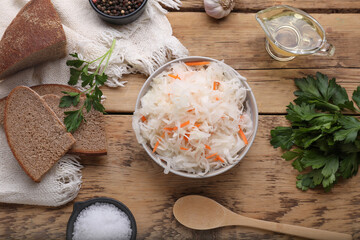 Bowl of tasty sauerkraut and ingredients on wooden table, flat lay