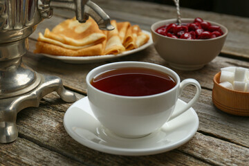 Metal samovar with cup of tea and treats on wooden table