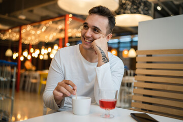 One man young adult Caucasian man sit at cafe or restaurant alone looking to the side having a cup of coffee real people copy space happy smile