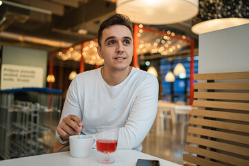 One man young adult Caucasian man sit at cafe or restaurant alone looking to the side having a cup of coffee real people copy space happy smile