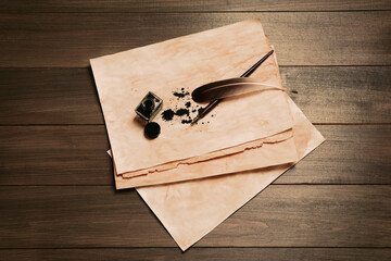 Feather, fountain pen, inkwell and vintage parchment with ink stains on wooden table, top view