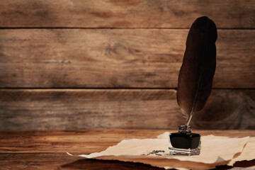 Inkwell with feather and vintage parchment with stains on wooden table. Space for text