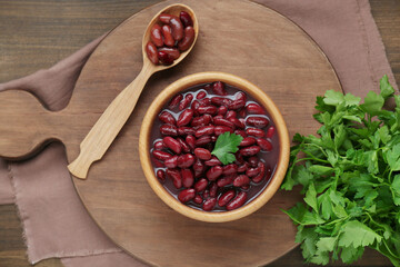 Bowl of canned red kidney beans, parsley and spoon on wooden table, flat lay