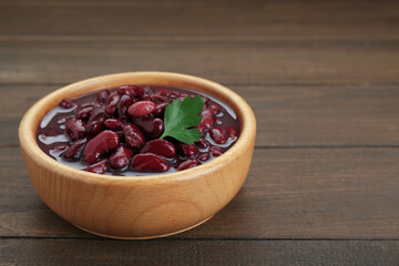 Bowl of canned red kidney beans with parsley on wooden table, closeup. Space for text