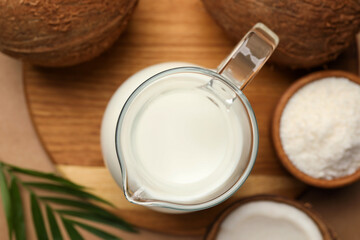 Glass jug of delicious vegan milk, coconuts and leaf on brown background, flat lay