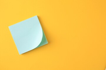 Blank paper note on orange background, top view. Space for text