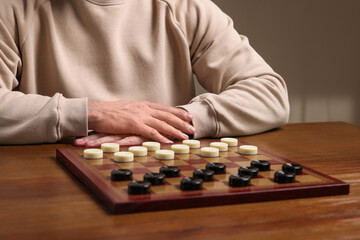 Playing checkers. Man thinking about next move at wooden table, closeup