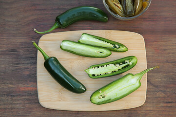 Fresh and pickled green jalapeno peppers on wooden table, flat lay