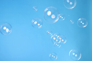 Many beautiful soap bubbles on light blue background