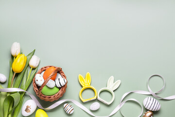 Flat lay composition with Easter eggs in basket and tulip flowers on pale olive background. Space...