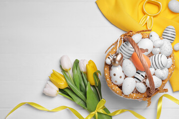 Flat lay composition with Easter eggs in basket and tulips on white wooden table. Space for text