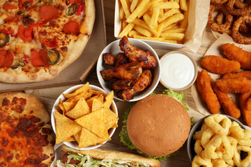 French fries, pizza and other fast food on wooden table, flat lay