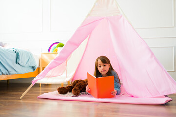 Cute girl enjoying reading a book in a tipi