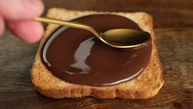 Сhocolate paste spreading on bread with a golden spoon, top view. Perfect traditional breakfast