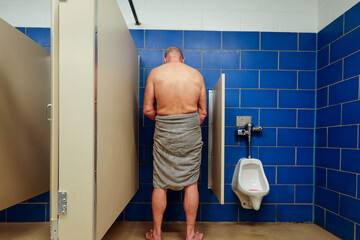 A man at a urinal in a public shower at a gym.