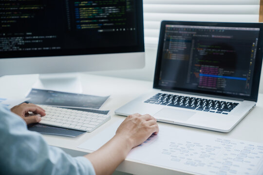 programmer writing program code with two monitors and working on a new software or hacker programming developing software applications in the office.