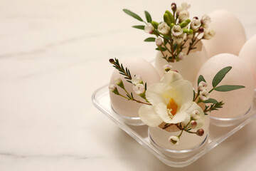 Easter eggs and beautiful flowers on white marble table, closeup. Space for text