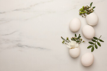 Easter eggs and beautiful flowers on white marble table, flat lay. Space for text
