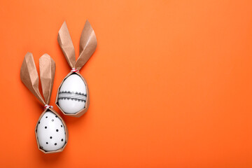 Easter bunnies made of craft paper and eggs on orange background, flat lay. Space for text