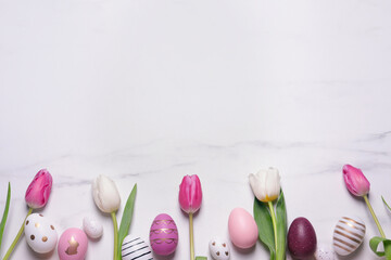 Flat lay composition of painted Easter eggs and tulip flowers on white marble table. Space for text