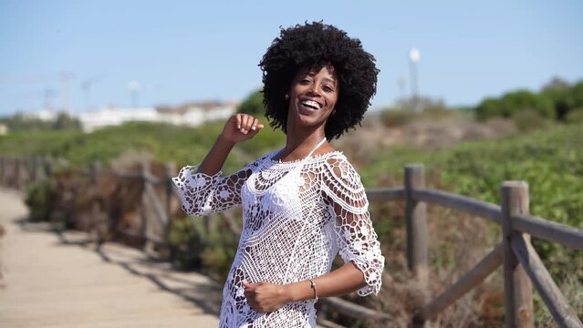 African American woman with afro hair, dancing on a wooden path near the beach