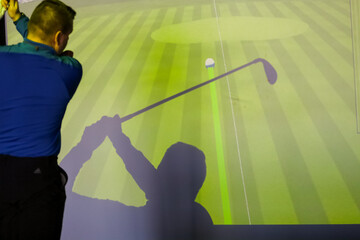 Man playing golf in front of the projector indoors. High quality photo