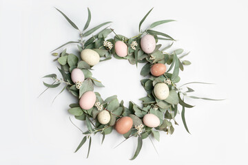 A beautiful Easter wreath made of eucalyptus leaves, delicate white flowers and pastel easter eggs, on a white background.