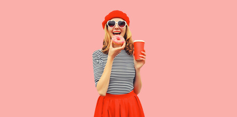 Portrait of happy cheerful young woman with eating sweet donut with cup of coffee or juice on pink...