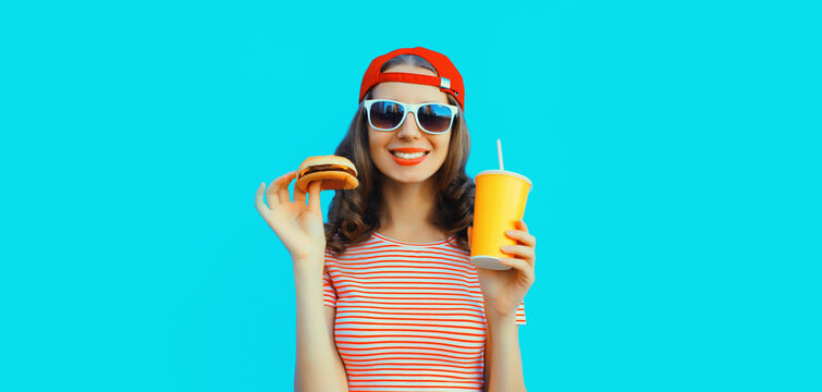 Portrait of stylish smiling young woman drinking juice with burger fast food on blue background