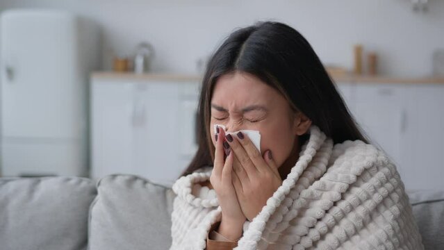 Sick Asian woman covered in blanket sneezing in paper napkin sneeze runny nose feel frozen cold unhealthy korean girl patient has covid symptom grippe nasal infectious disease health treatment at home