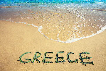 Inscription GREECE on a sandy beach with sea waves. Nature background