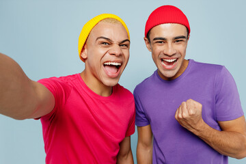 Close up young couple two friends men wear casual clothes look camera together doing selfie shot pov on mobile cell phone do winner gesture isolated on pastel plain light blue cyan background studio.