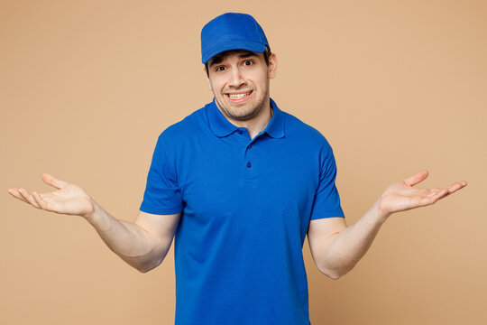 Sad delivery guy employee man wear blue cap t-shirt uniform workwear work as dealer courier spread hands shrugging shoulders looking puzzled isolated on plain light beige background. Service concept.