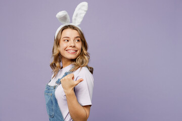 Side view fun young woman wear casual clothes bunny rabbit ears pointing aside indicate on workspace area copy space isolated on plain pastel purple background studio. Lifestyle Happy Easter concept.