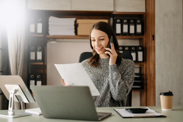 Business asian woman Talking on the phone and using a laptop with a smile while sitting at office.