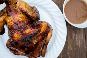 Lechon Manok, or roasted chicken served outside at a bench with gravy.